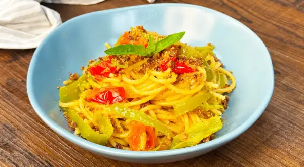Spaghetti con friggitelli, pomodorini e mollica tostata, guarniti con basilico fresco. Un piatto semplice e gustoso.
