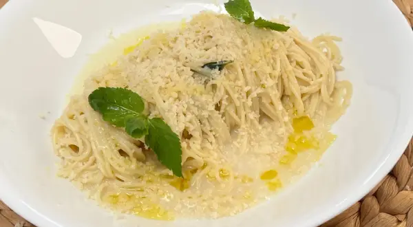 Spaghetti al limone, conditi con parmigiano grattugiato, olio d'oliva e guarniti con foglie di menta fresca.