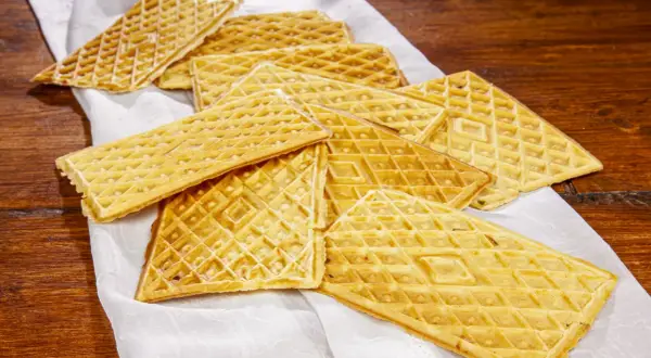 Un mucchio di croccanti ferratelle abruzzesi, dolci tradizionali dorati, disposte su un panno bianco su un tavolo di legno.