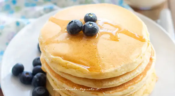 Pancakes senza glutine dorati, impilati e guarniti con mirtilli freschi e sciroppo d'acero.