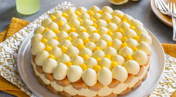 Delizioso tiramisù al limoncello, con strati di savoiardi, crema al limone e decorazioni di panna e cubetti di limone.