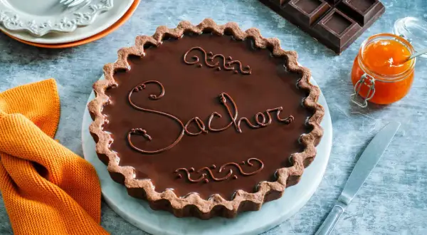 Una crostata Sacher lucida e invitante, con decorazioni in cioccolato e un vasetto di marmellata d'arancia accanto.