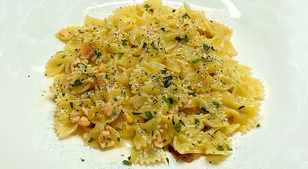 Farfalle condite con cubetti di salmone rosa, prezzemolo tritato e pepe nero. Un piatto di pasta al salmone invitante.
