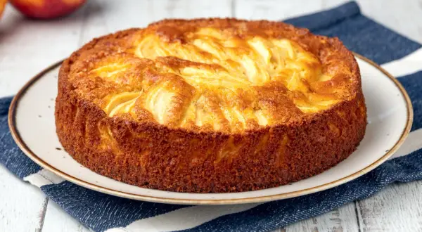 Una deliziosa torta di mele dorata, con mele a vista sulla superficie, servita su un piatto con un tovagliolo a righe blu.