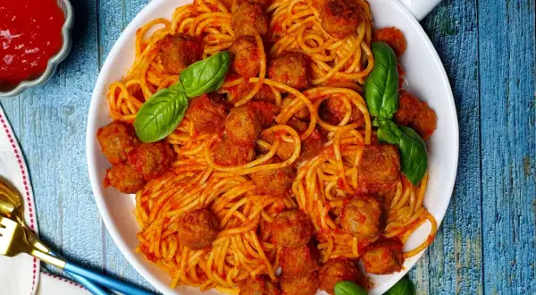 Un piatto invitante di spaghetti con polpette, conditi con salsa rossa e guarniti con foglie di basilico fresco.