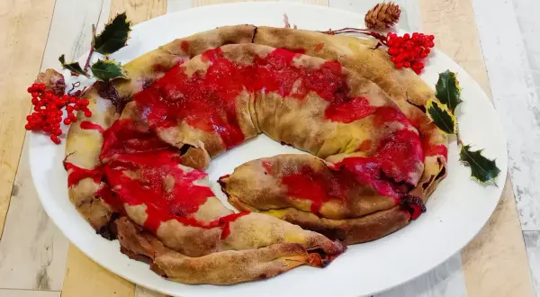 Dolce natalizio a forma di spirale, una rocciata umbra con glassa rossa e decorazioni di agrifoglio e bacche.