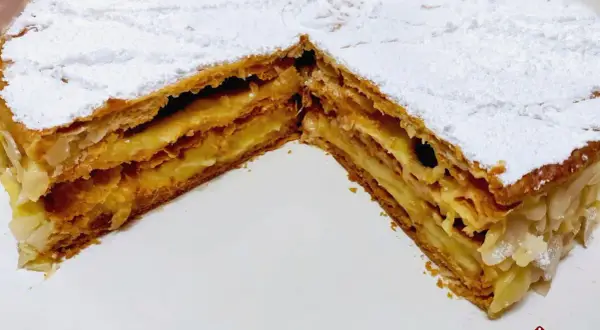 Una fetta di torta millefoglie con crema pasticcera e mandorle, cosparsa di zucchero a velo.