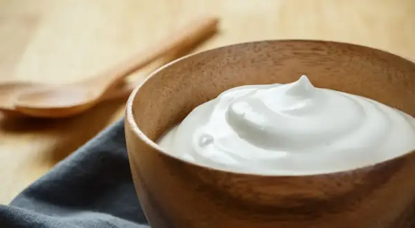 Una ciotola di legno piena di soffice crema di latte, perfetta per la tua prossima ricetta. Due cucchiai di legno sullo sfondo.