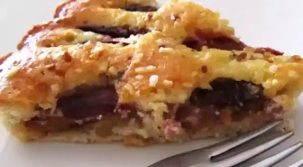 Una fetta di torta con prugne fresche, con crosta dorata e ripieno succoso, pronta per essere gustata.