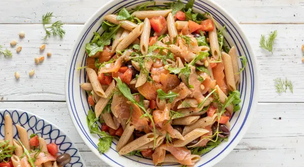 Pasta fredda con salmone affumicato, pomodorini, rucola e olive nere. Un piatto estivo leggero e gustoso.