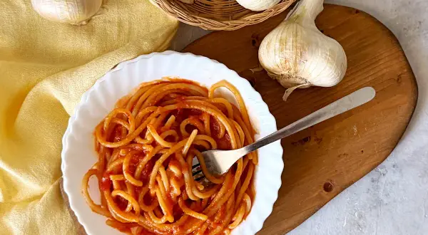 Piatto di pici all'aglione fumanti, con aglio fresco in primo piano. Un classico della cucina toscana.
