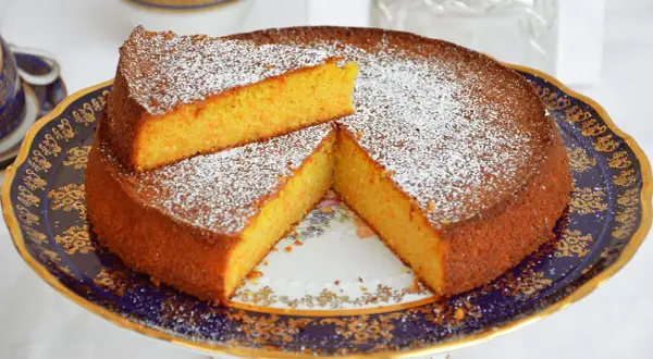 Una deliziosa torta carote e mandorle, spolverata di zucchero a velo, servita su un elegante piatto blu e oro.