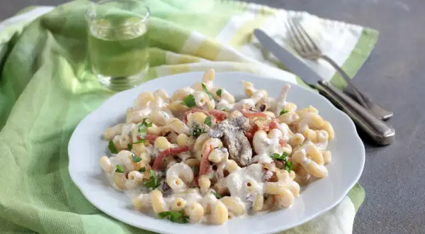 Piatto di pasta alla boscaiola cremosa con funghi e pancetta, guarnita con prezzemolo fresco.