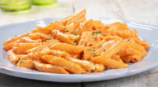 Penne cremose con salsa rosa, un classico tra le pasta ricette, guarnite con prezzemolo e parmigiano.
