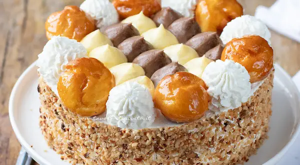 Una magnifica torta Saint Honoré, decorata con bignè caramellati, ciuffi di panna montata e crema pasticcera al cioccolato e vaniglia.