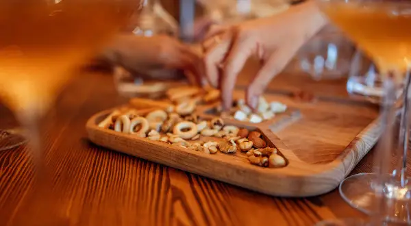 Un vassoio di legno con taralli e frutta secca, accanto a bicchieri di vino ambrato. Un momento di relax e gusto.