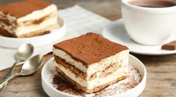 Delizioso tiramisù, perfetto per la tua tiramisù ricetta benedetta. Servito su un piatto bianco con caffè e cucchiaini.