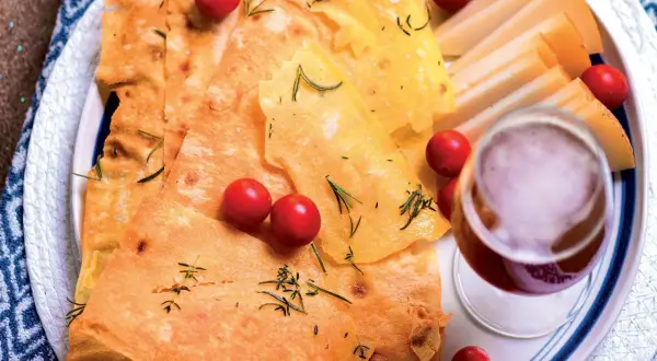 Pane guttiau croccante con pomodorini, rosmarino e fette di formaggio, accompagnato da un bicchiere di vino rosso.