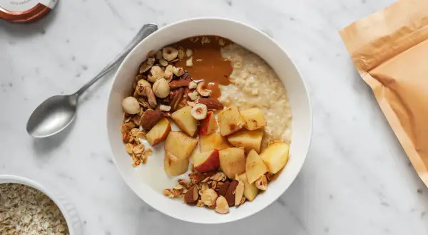 Una ciotola di avena per colazione con mele, frutta secca e burro di arachidi. Un pasto sano e gustoso.