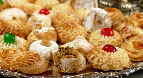 Vassoio pieno di dolcetti invitanti, tra cui spiccano le paste di mandorla decorate con ciliegie candite e granella di pistacchio.