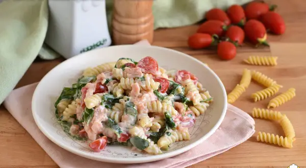 Piatto di pasta fredda con salmone, pomodorini e rucola, condita con una cremosa salsa.