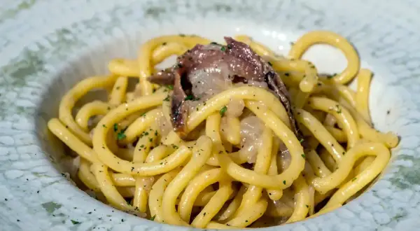 Un piatto di bigoli in salsa, con pasta spessa e condimento saporito, guarnito con prezzemolo tritato.