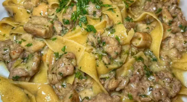 Pappardelle cremose con salsiccia e funghi, guarnite con prezzemolo fresco. Un piatto ricco e saporito.