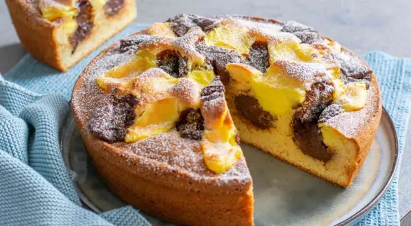 Torta nua con crema pasticcera e cacao, spolverata di zucchero a velo. Una fetta è già stata tagliata, rivelando il morbido interno.