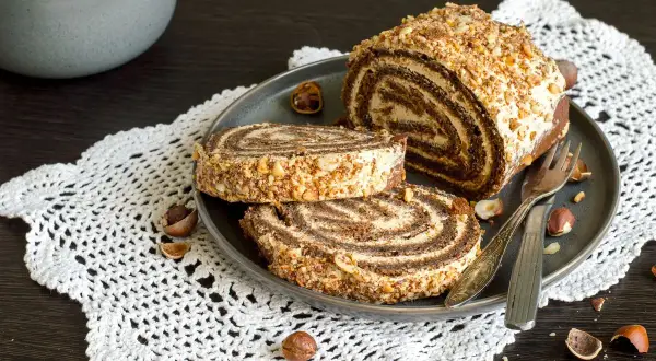 Un delizioso rotolo alla Nutella, ricoperto di granella di nocciole, servito su un piatto con due fette tagliate.