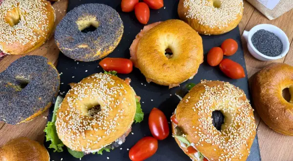Varietà di bagel, alcuni con semi di sesamo, altri con semi di papavero, pronti per una deliziosa bagel ricetta. Pomodorini e salmone completano la scena.