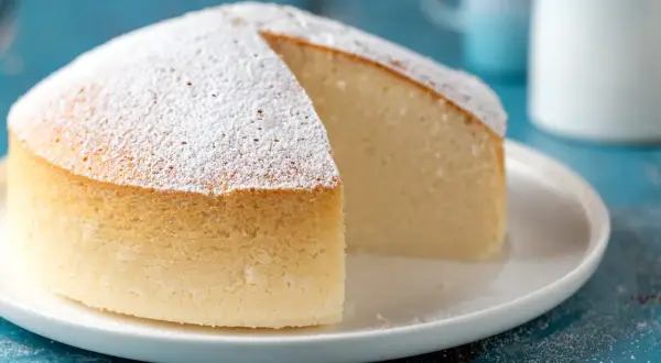 Una soffice torta nuvola, cosparsa di zucchero a velo, su un piatto bianco. La sua consistenza leggera invita a un morso goloso.