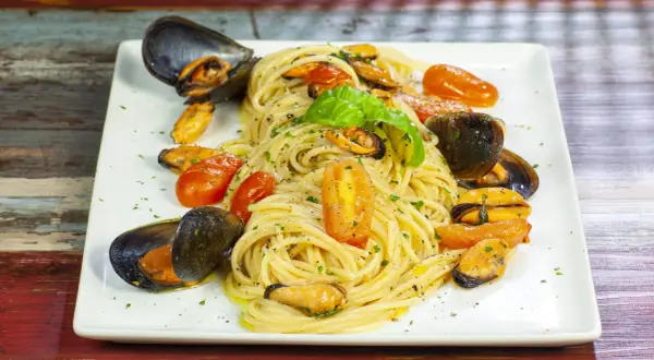 Un invitante piatto di spaghetti con le cozze e pomodorini, guarnito con basilico fresco.