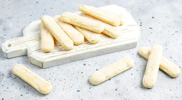 Savoiardi pronti per la ricetta del tiramisù, disposti su un tagliere bianco.