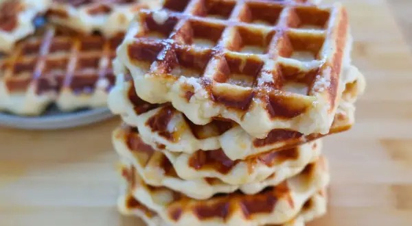 Una pila di waffle dorati, con la loro tipica griglia, che ricordano la waffle ricetta originale belga.