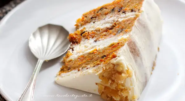 Una fetta di torta di carote, soffice e ricca, con glassa bianca e noci tritate.