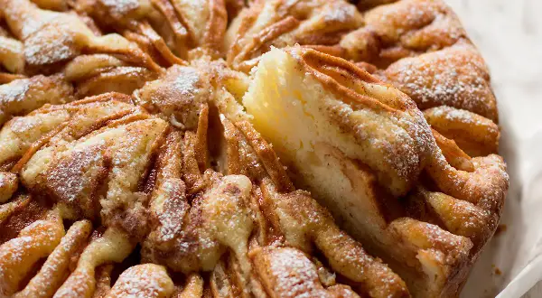 Una fetta di torta di mele morbidissima, cosparsa di zucchero a velo, con un aspetto invitante e casalingo.
