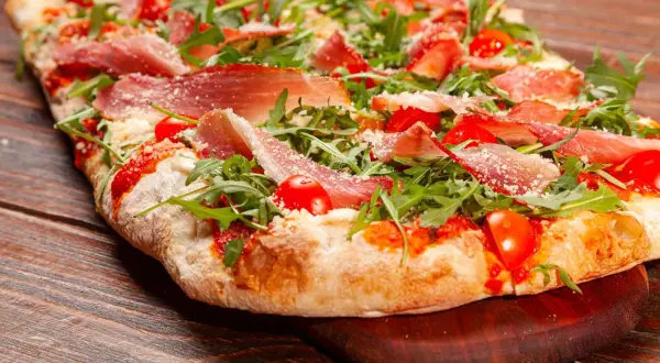 Pizza bianca con prosciutto crudo, pomodorini e rucola, cosparsa di parmigiano. Un'esplosione di sapori su un impasto soffice.