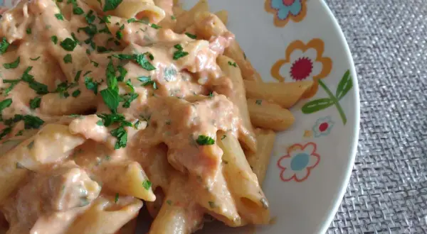 Penne al baffo cremose e gustose, condite con un sugo rosato e prezzemolo fresco, servite su un piatto decorato con fiori colorati.