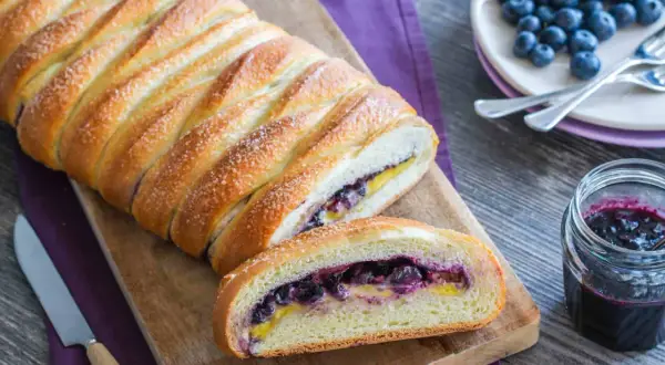 Una deliziosa treccia mochena ripiena di mirtilli e crema, cosparsa di zucchero, pronta per essere gustata.