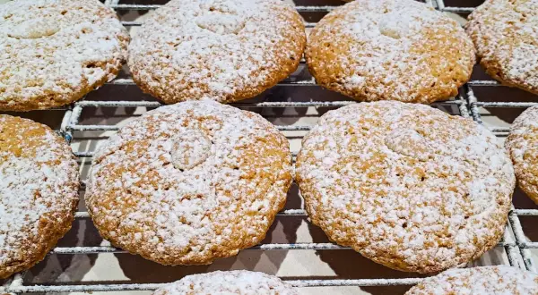 Biscotti con farina di mandorle, cosparsi di zucchero a velo, riposano su una griglia.