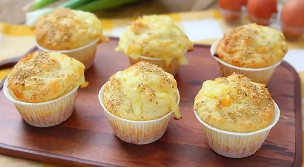 Sei muffin salati dorati, guarniti con semi di sesamo e formaggio filante, pronti per essere gustati.
