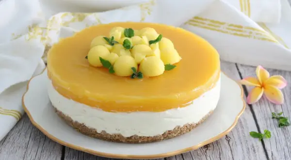 Cheesecake al mango con palline di frutta e menta fresca, su una base croccante. Un dolce estivo invitante.