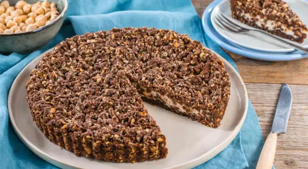 Sbriciolata ricotta e cioccolato con croccante copertura di nocciole e cacao. Una fetta è già servita su un piattino.