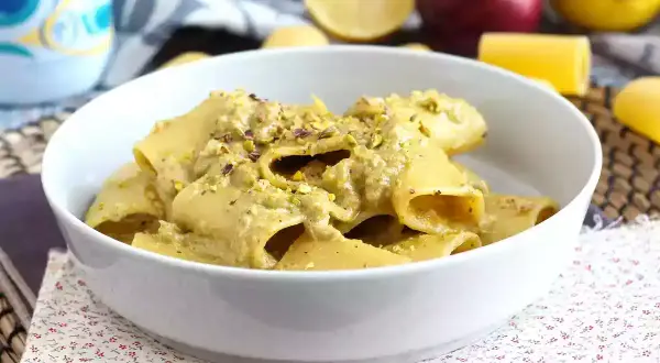 Piatto di pasta tonno e limone, condita con una crema verde e pistacchi tritati, servita in una ciotola bianca.