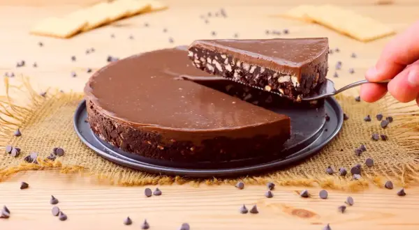 Una fetta di golosa torta fredda al cioccolato, con biscotti sbriciolati e una lucida glassa, viene sollevata da una paletta.
