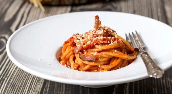 Un piatto di spaghetti alla amatriciana, con guanciale croccante e un tocco di cipolla per una ricetta originale.