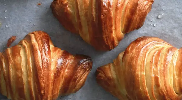Cornetti dorati e sfogliati, perfetti per la ricetta cornetti fatti in casa. Si intravedono gocce d'acqua sulla carta da forno.
