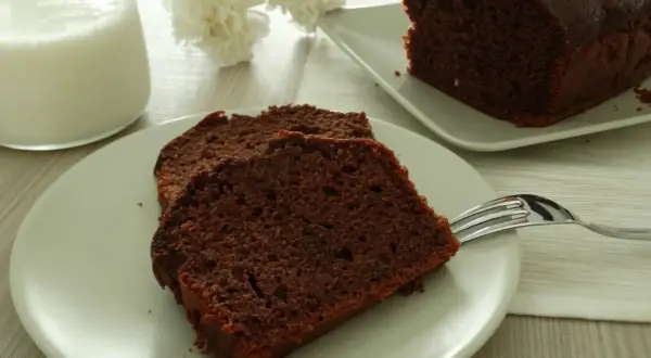 Fette di plumcake al cioccolato su un piatto, con una forchetta e un bicchiere di latte sullo sfondo.