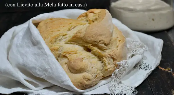 Pane senza lievito di birra, dorato e fragrante, avvolto in un panno bianco. Accanto, un vasetto con lievito madre alla mela.