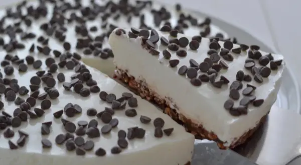 Una fetta di torta fredda allo yogurt, ricoperta di gocce di cioccolato, viene servita da una spatola.